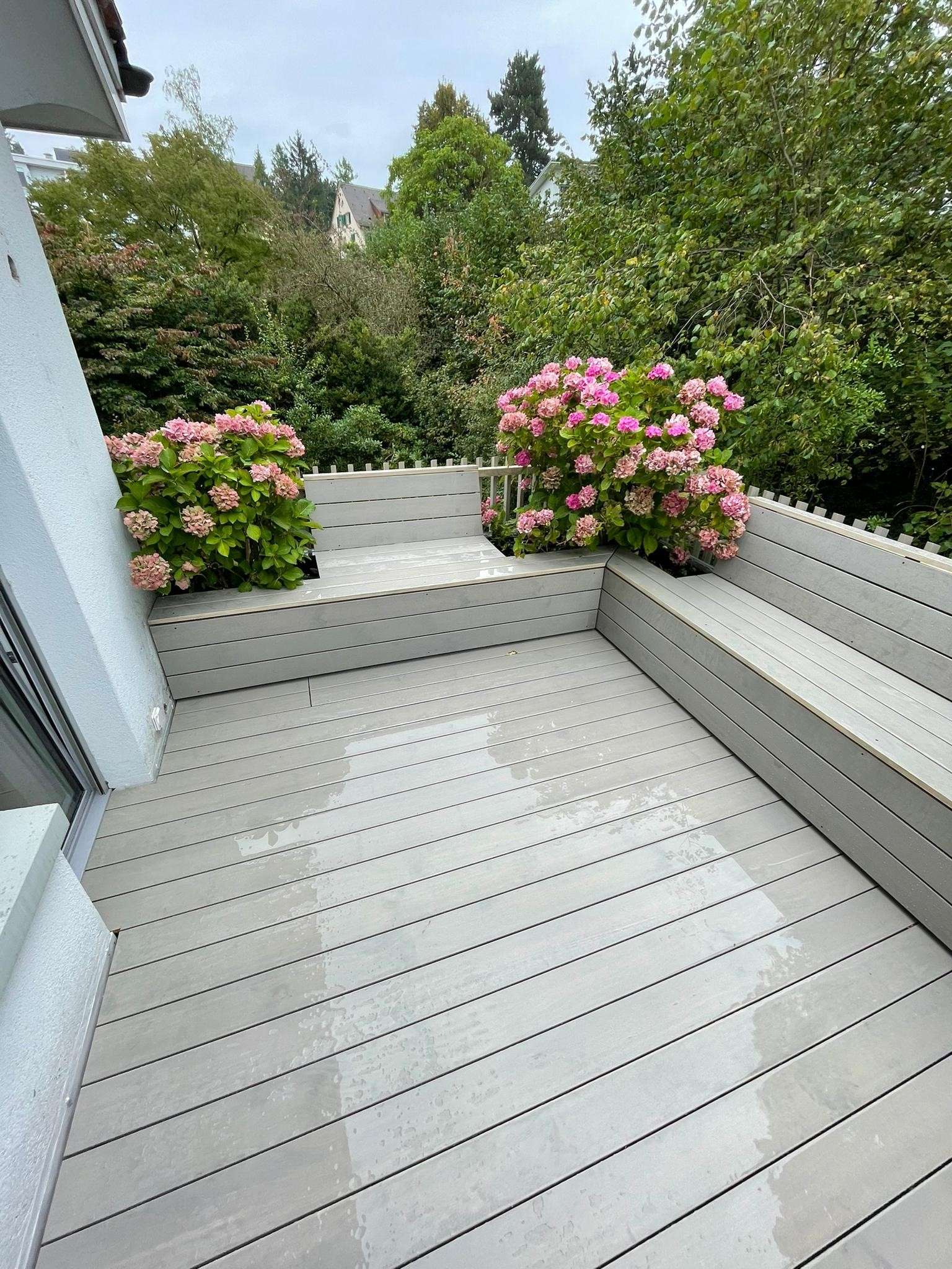 Terrasse aus Accoya Holz mit Vor-Vergrauungslasur, ergänzt durch eine integrierte Treppe, ein passendes Holzgeländer und eine Sitzbank; modernes, hochwertig verarbeitetes Aussenprojekt.