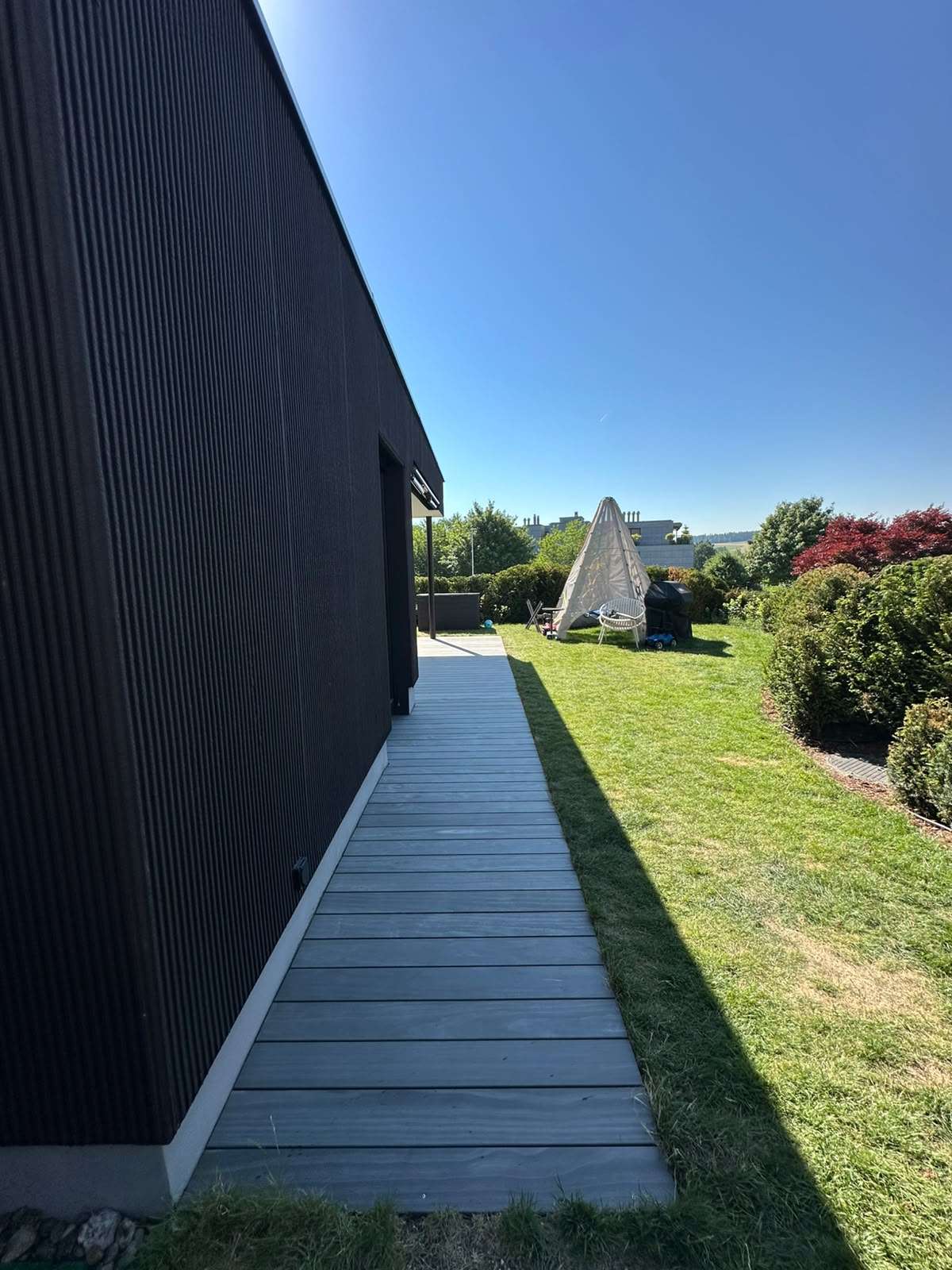Moderne Accoya Terrasse aus Accoya Grey mit grauen Terrassendielen vor einem schwarzen Einfamilienhaus und überdachtem Sitzbereich.