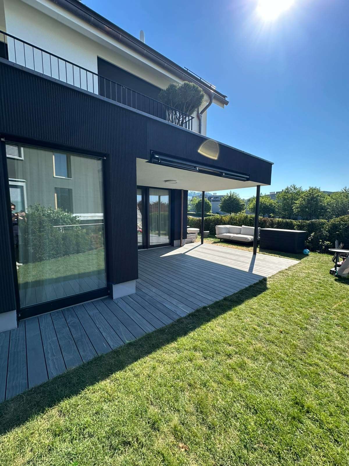 Moderne Accoya Terrasse aus Accoya Grey mit grauen Terrassendielen vor einem schwarzen Einfamilienhaus und überdachtem Sitzbereich.